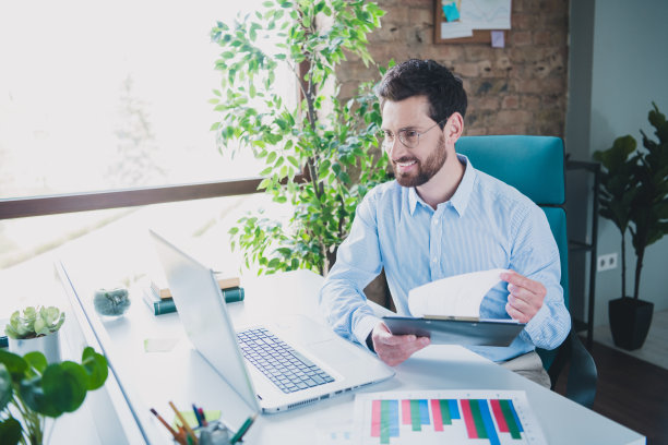 年轻男性在现代办公室中穿着时尚的正式服装，在线会议中阅读报告的照片肖像，展现成功的企业主形象。图片下载
