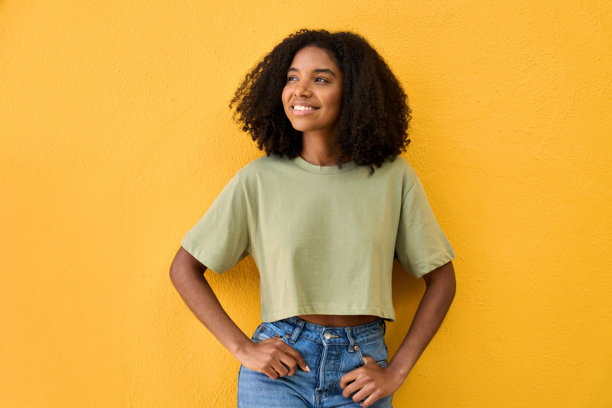 快乐的年轻非裔美国人Z世代女孩站在黄色墙前，目光投向远方。图片下载