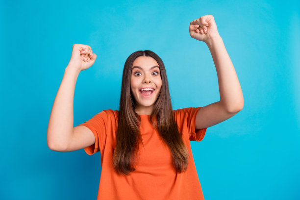 可爱的少女穿着时尚的橙色服装，在蓝色背景下庆祝获胜的照片肖像图片下载