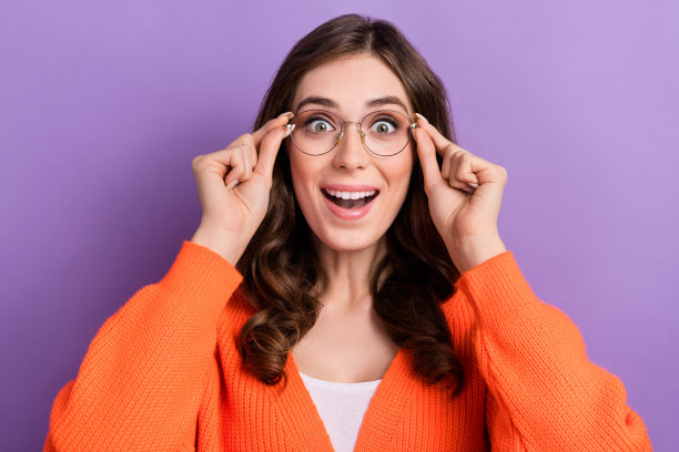 年轻女图书管理员近距离照片，视力不佳，尝试新眼镜，惊讶的反应，高质量镜片，背景为紫色。图片下载
