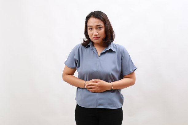 亚洲女性因月经疼痛而感到腹部不适，弯腰并用手捂住肚子。图片下载