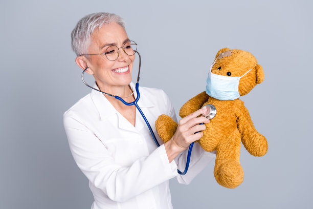 穿着白大褂的迷人儿科医生，手持玩具，背景为灰色。图片下载