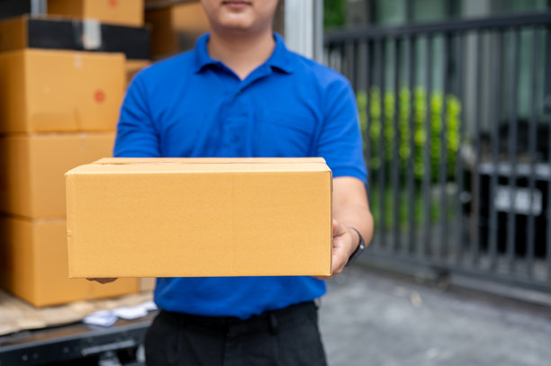 一张裁剪过的图片，显示一名送货员站在卡车后面，手里拿着一个待送的包裹。图片下载