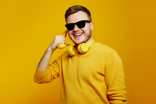搞笑的男人穿着黄色毛衣和太阳镜，手里拿着香蕉像手机一样靠在耳边微笑。图片下载