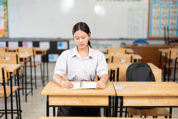 一位长发的亚洲女学生穿着校服走进教室，手里拿着一本书，准备在学校开始充实的一天学习，汲取丰富的知识。图片下载