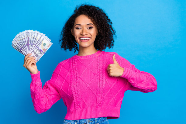 照片中，可爱自信的女士穿着粉红色的套头衫，竖起大拇指，背景是孤立的蓝色图片下载