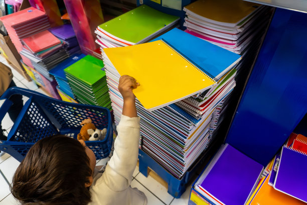 一个孩子在商店里伸手去拿一本黄色的螺旋笔记本图片下载