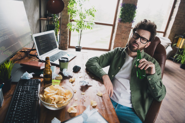 年轻男性IT专家在室内阁楼办公室的电脑桌上摆放着啤酒瓶的照片图片下载