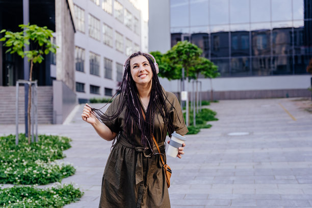 一位女性在街上戴着耳机跳舞，同时喝着早晨的咖啡。图片下载