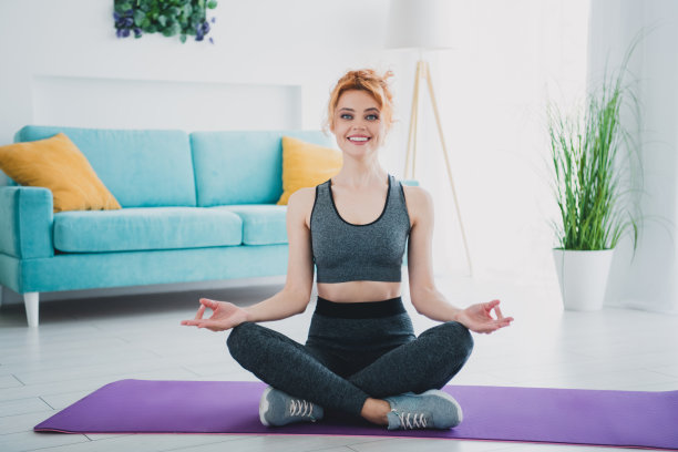 全身照片，年轻漂亮的运动女性在家中的健身房瑜伽垫上冥想。图片下载