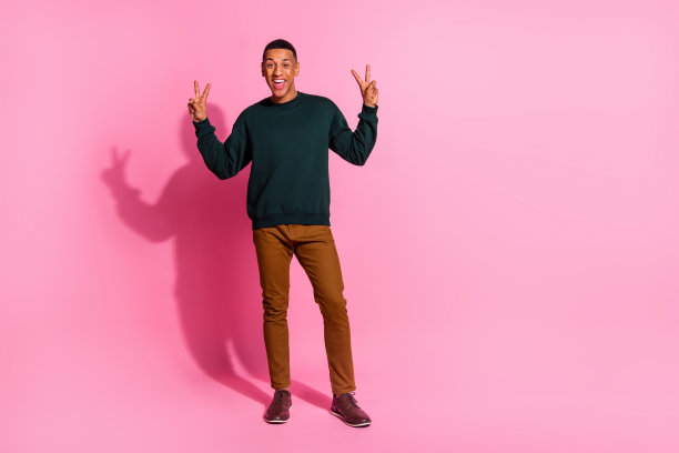 时髦酷的家伙穿着套头衫的全长照片，显示了两个v字的空白空间孤立的粉红色背景图片下载