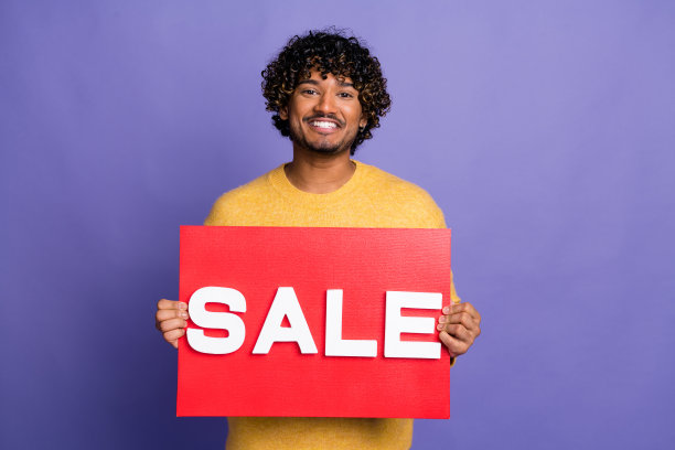 照片中开朗的拉丁男子穿着时髦的黄色衣服，手臂拿着红色的标语牌，在紫色的背景上孤立的出售新闻图片下载