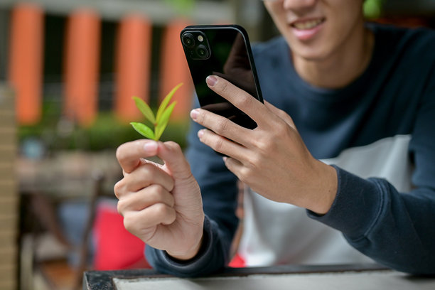 一张裁剪过的图片，一名亚洲男子拿着他的智能手机和一张绿叶放在桌子上。图片下载