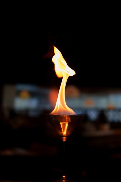 一张迷人的照片，展示了一只装满酒精的马提尼酒杯，上面燃烧着跳动的火焰。图片下载