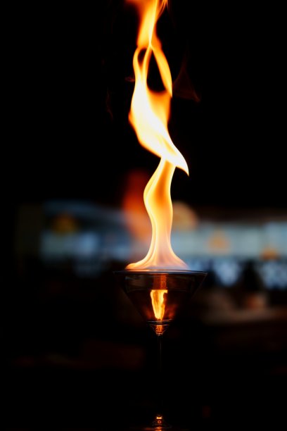 一张迷人的照片，展示了一只装满酒精的马提尼酒杯，上面燃烧着跳动的火焰。图片下载