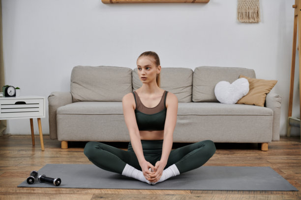 年轻女性穿着舒适的运动服在家锻炼，倡导健康与养生图片下载