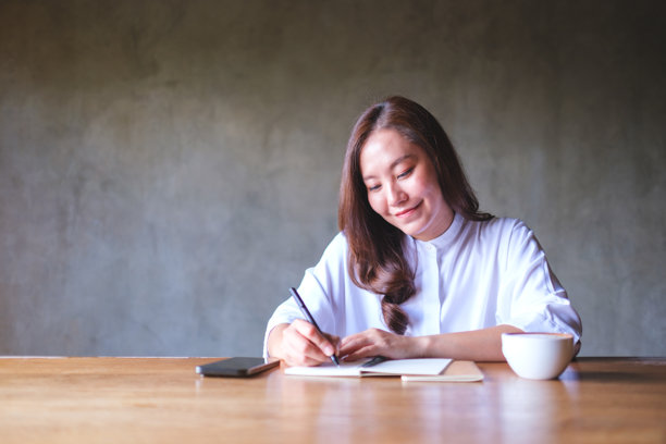 一位女性在木桌上写笔记，旁边有手机和咖啡杯的肖像照片图片下载