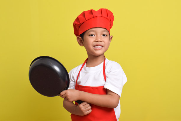 可爱的小厨师手持煎锅和铲子。一个穿着红色围裙的亚洲男孩。图片下载