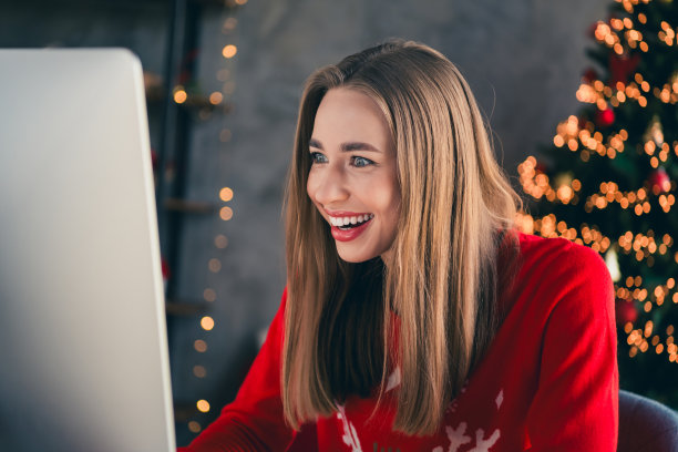 年轻女孩兴奋地看着显示器，穿着圣诞服装，享受现代舒适的圣诞派对装饰，室内公寓环境。图片下载