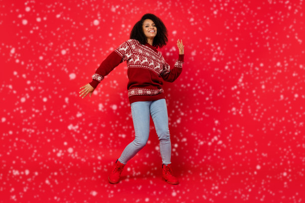 穿着毛衣的女性在圣诞派对上微笑跳舞，背景为明亮的红色，整身照片。图片下载