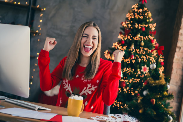 穿着圣诞服装的可爱快乐女孩在室内房间里使用电脑，享受传统节日气氛的装饰。图片下载