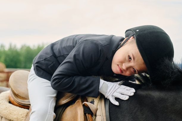 年轻男孩坐在马鞍上抚摸马匹图片下载