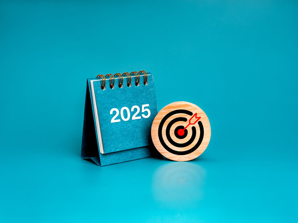 2025年新年快乐最小横幅。圆形木块上的目标图标和蓝色小台历封面上的白色2025数字孤立地站在蓝色背景上。经营目标和成功理念。图片下载