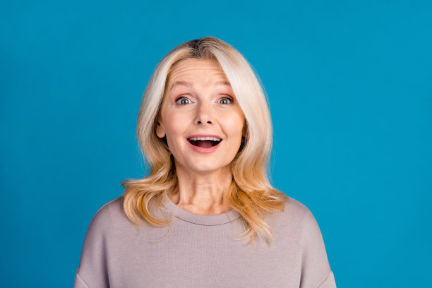 可爱的高级女士的照片肖像微笑着看着相机惊讶地穿着时尚的灰色服装孤立的蓝色背景图片下载