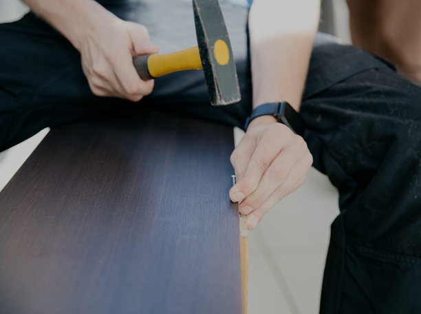 一个年轻人正在用锤子修理一个旧橱柜。图片下载