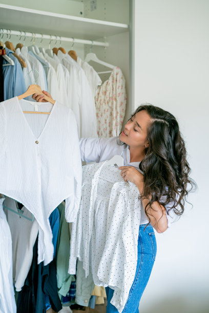 年轻的黑发卷发美丽女性正在整理宽敞的大衣橱。家庭整理。清洗物品。按季节分析衣物。图片下载