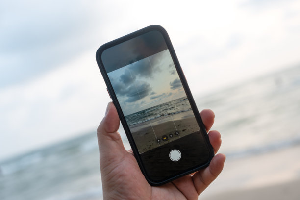 男人在日落时分的海滩上用手机拍照图片下载