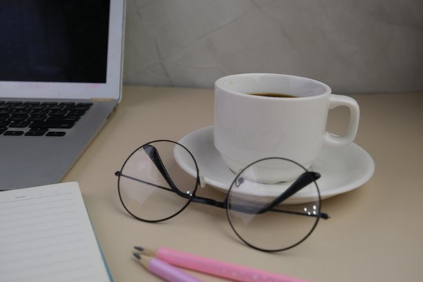 灰色桌子上的工作场所平铺，摆放着一杯咖啡、一台笔记本电脑和一本笔记本。教育、商业和办公室概念。图片下载