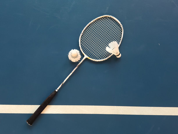 室内羽毛球场上，暗色地板上有奶油白色的羽毛球和球拍，配有霓虹灯光影，留有空白，柔和且选择性对焦。图片下载