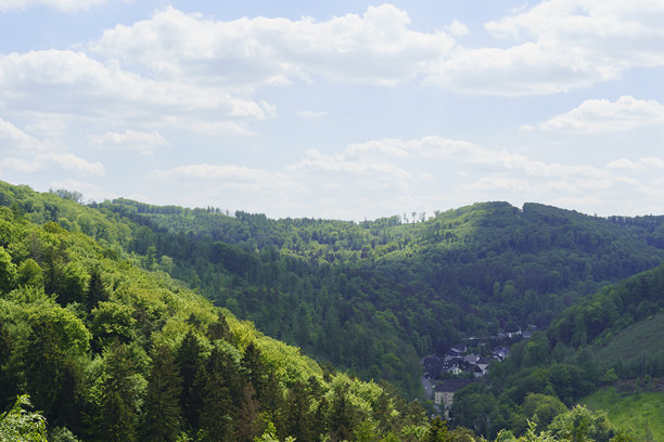 白色厚厚的云朵在蓝天上漂浮，覆盖着绿色的丘陵和树木茂密的地表。这是一张美丽的德国风景照片。图片下载
