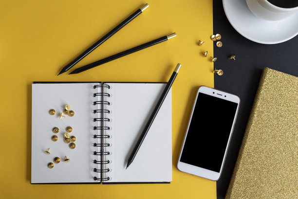 办公桌上有螺旋笔记本、铅笔、带屏幕的智能手机和咖啡杯。黄色背景上的办公用品。工作场所。网页横幅。图片下载