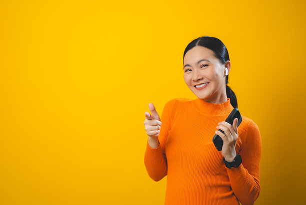 亚洲女性享受使用智能手机，戴着耳机听音乐，背景为单色。图片下载