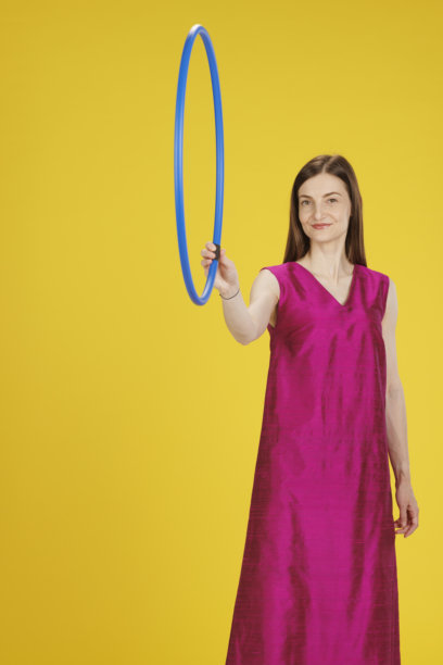 充满活力的肖像，优雅的女商人正在练习呼啦圈。紫红色丝绸裙子，优雅的生活方式。黄色背景。图片下载