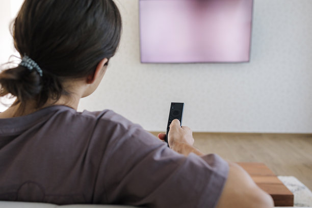 是时候看电视了。一个少年男孩使用遥控器打开电视，观看某个节目。大屏幕。图片下载
