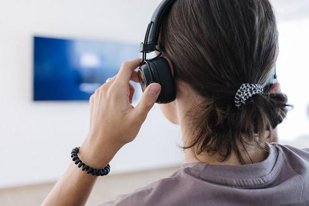 少年从背面戴上无线耳机，并将其连接到电视上观看节目。图片下载