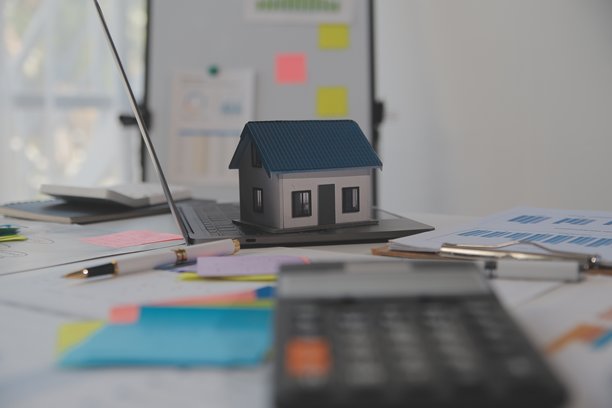 木桌上放着笔记本电脑、房屋钥匙、带笔的剪贴板、房屋模型和绿色树木计算器，房地产概念。特写照片。图片下载