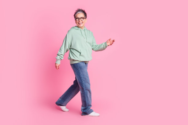 穿着卡其色连帽衫的快乐女士在粉色背景的空旷空间中行走的全身照片图片下载