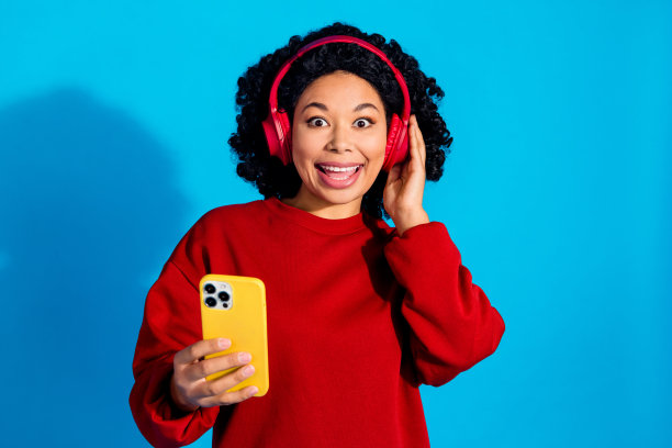 时尚红色服装的可爱年轻女士佩戴耳机的照片肖像，背景为蓝色。图片下载