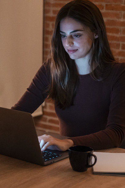 年轻女商人在家中的办公室里工作，晚上使用笔记本电脑进行商务活动和赚钱。这张照片展示了远程办公和智能工作的场景，现代女性在管理任务。图片下载