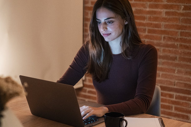 年轻女商人在家中的办公室里工作，晚上使用笔记本电脑进行商务活动和赚钱。这张照片展示了远程办公和智能工作的场景，现代女性在管理任务。图片下载