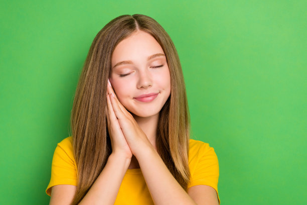 年轻女孩学生在绿色背景下双手合十，闭眼放松，学习后小憩的特写照片图片下载