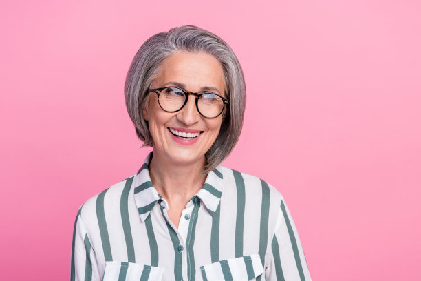 成熟退休女商人的照片肖像，微笑着看向空旷的空间，佩戴眼镜，适用于新公司广告，背景为粉色。图片下载