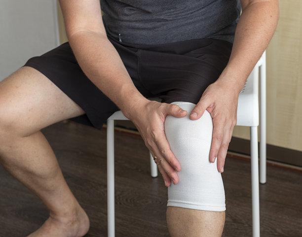 男子坐在白色椅子上，手扶膝盖，右膝盖上缠着弹性绷带的健康护理照片图片下载
