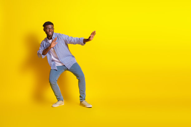 穿着格子衬衫的时尚酷男士在空旷的黄色背景下练习空手道的全身照片图片下载