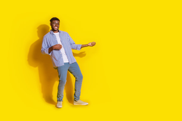 穿着格子衬衫的时尚酷男士在黄色背景下伸展双臂，身处空旷空间的全身照片图片下载