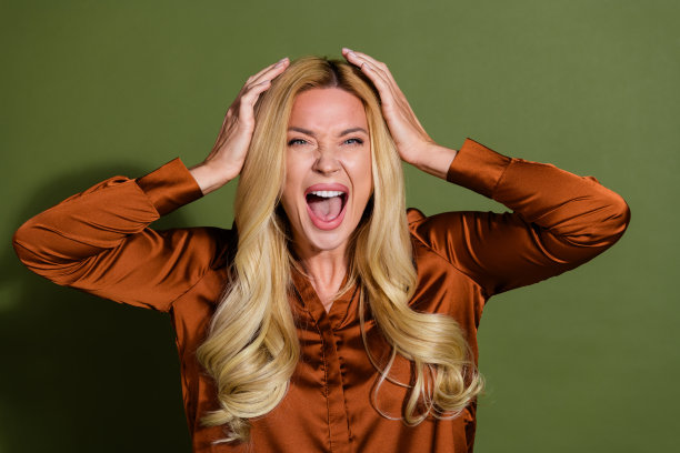 穿着时尚缎面衣服、声音响亮的惊讶疯狂女性照片，背景为卡其色。图片下载